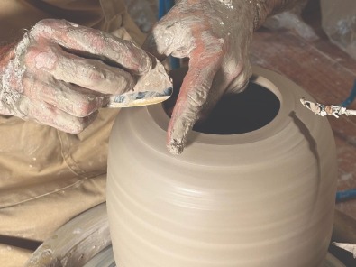les mains du tourneur en céramique sur les lèvres de l'urne entrain de faire les finitions de la pièce avec son esthèque